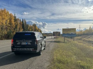 BC Highway Patrol ghost cruiser with emergency lights on beside a Highway 97 construction zone sign near Prince George