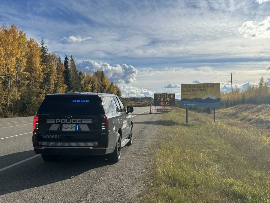 BC Highway Patrol ghost cruiser with emergency lights on beside a Highway 97 construction zone sign near Prince George