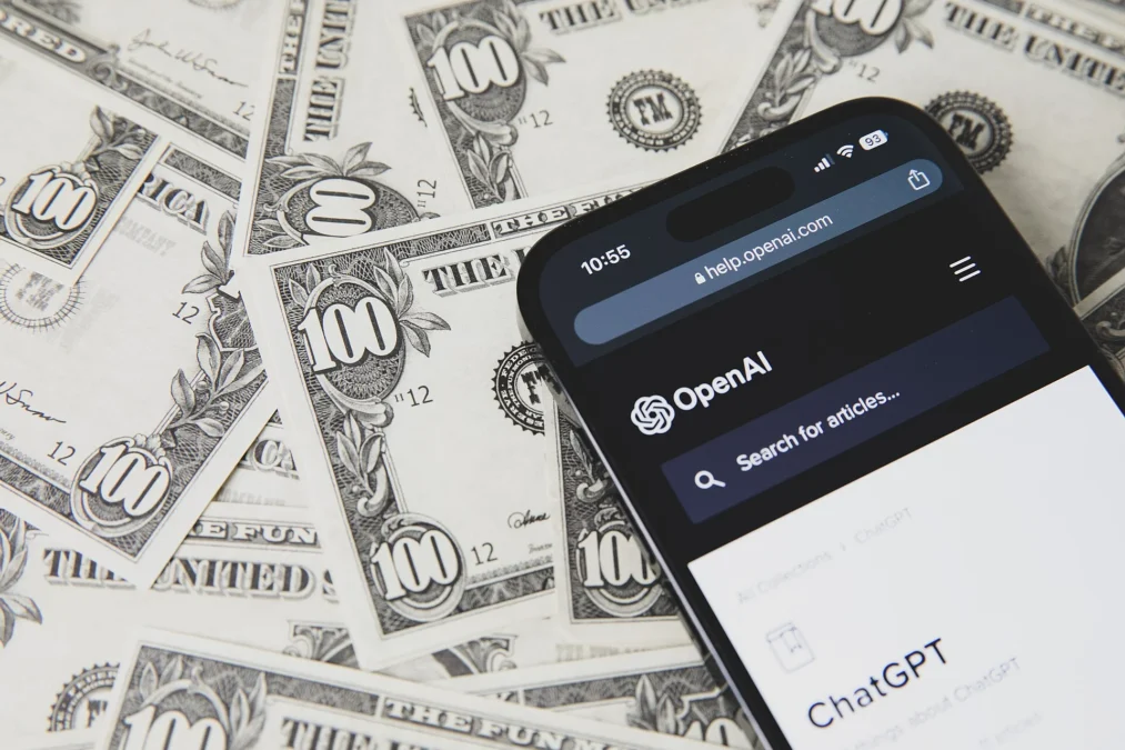 Phone showing OpenAI and ChatGPT resting on United States dollar banknotes