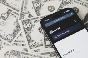 Phone showing OpenAI and ChatGPT resting on United States dollar banknotes