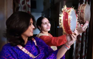 Two women in traditional dress holding decorated sieves up to view the moon during the Karwa Chauth ritual