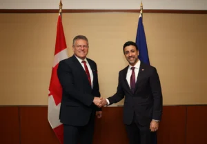 Maroš Šefčovič and Maninder Sidhu shaking hands in front of Canada and EU flags